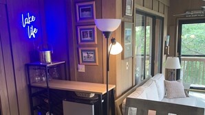 Ein gemütliches Zimmer mit einem Neon-Schild mit der Aufschrift „Lake Life“, einem Holztisch mit Lampe, einer Couch mit Kissen und gerahmten Bildern an der Wand.