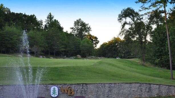 Ein Springbrunnen in einem Gewässer mit einer Steinmauer und einem Golfplatz im Hintergrund.