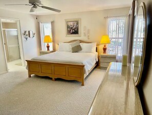 A bedroom with a bed, bedside lamps, a ceiling fan, a painting, and a window with curtains.
