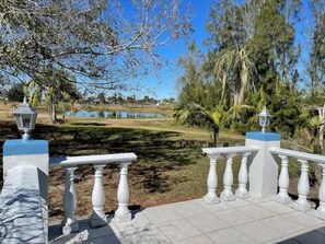 A serene outdoor area with a stone pathway, white balustrades, and a pond in the background.