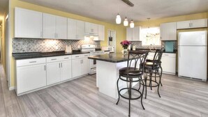 Une cuisine moderne avec des meubles blancs, un plan de travail en granit et un îlot central doté de tabourets de bar.