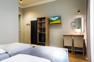 Quarto com duas camas, televisão na parede, escrivaninha com cadeiras e espelho.