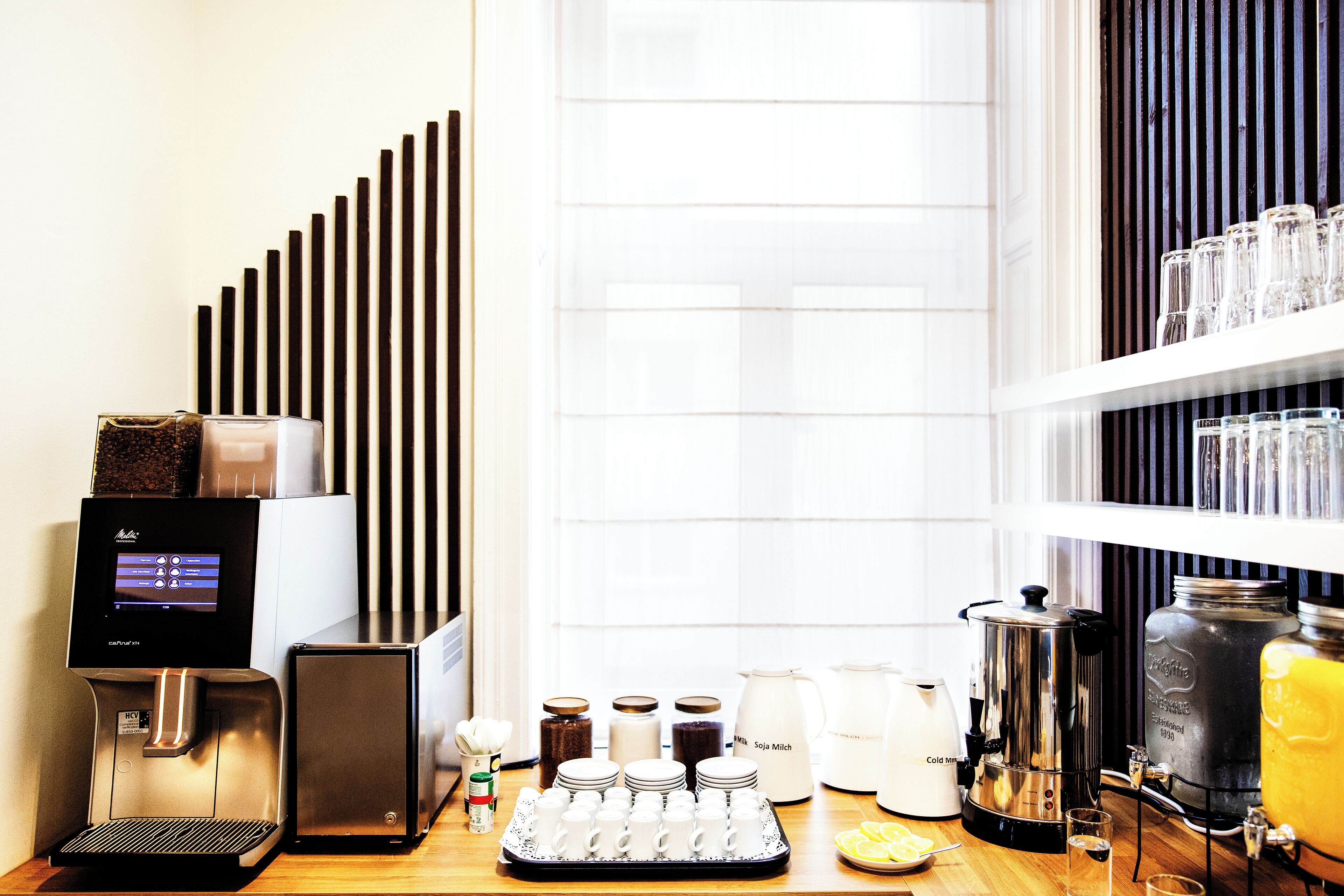 A coffee station with a coffee machine, milk frother, and various coffee containers.