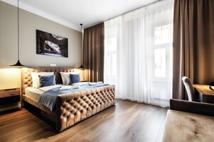 Quarto com cabeceira estofada, cama grande, mesa de cabeceira, escrivaninha e uma cadeira.