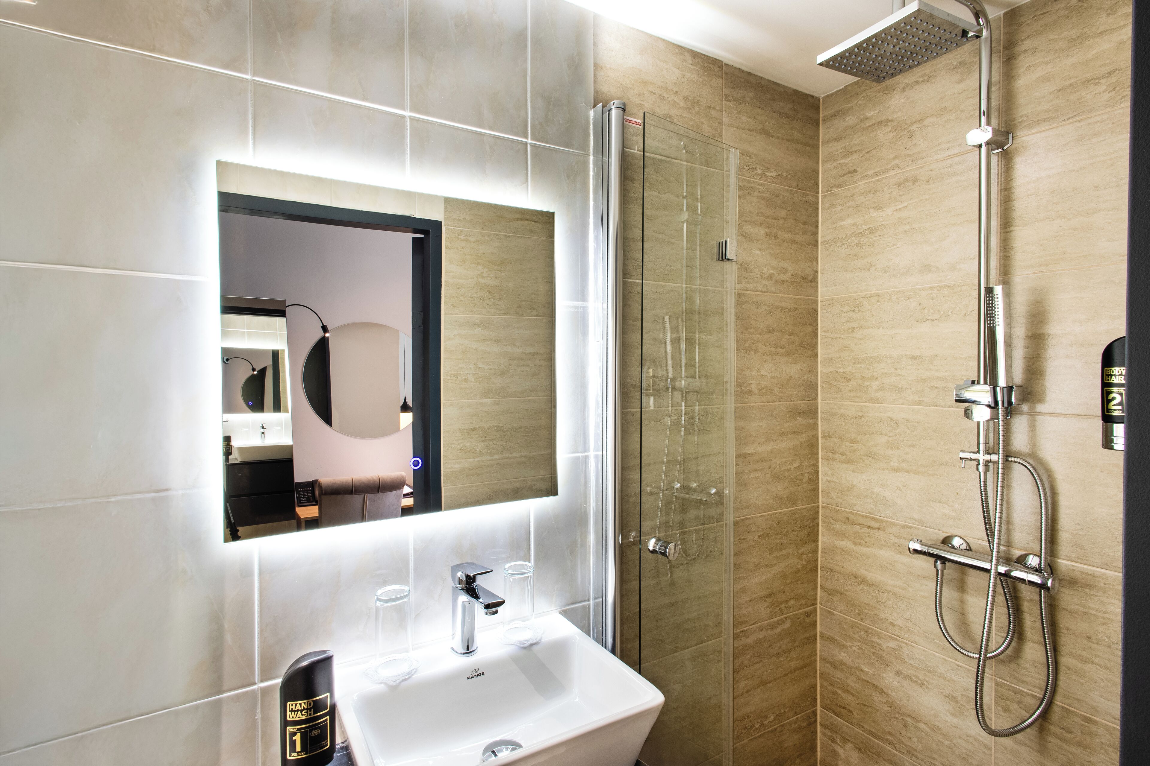 A modern bathroom with a glass shower enclosure, a white sink, and a large mirror.