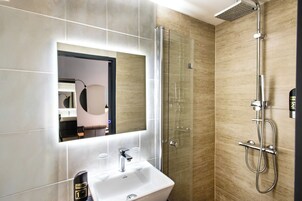 Un baño moderno con cabina de ducha de vidrio, un lavamanos blanco y un espejo grande.