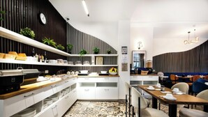 A modern kitchen with white cabinets, a wooden countertop, and a variety of kitchen appliances. There is a dining area with a table set for two and a seating area with chairs. - Vayalen Boutiquehotel  (Vienna)