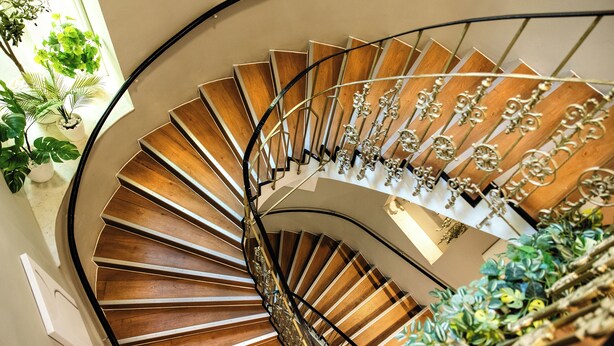 A spiral staircase with wooden steps and ornate metal railings, surrounded by potted plants. - Vayalen Boutiquehotel  (Vienna)