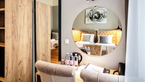 A hotel room with a wooden wardrobe, a round mirror reflecting a bed and a sofa, a desk with a telephone, and a wall-mounted light fixture. - Vayalen Boutiquehotel  (Vienna)