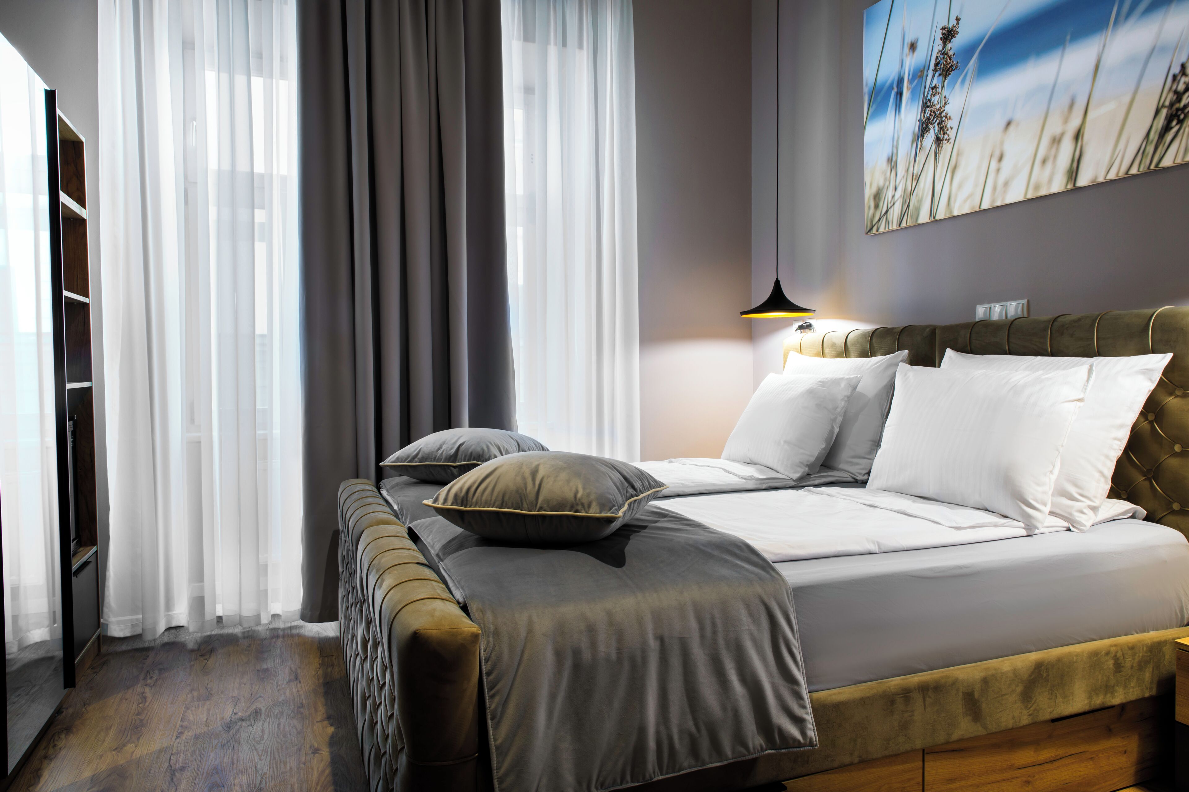 A bedroom with a bed, a bedside table, a lamp, and a large window with curtains.