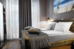 Quarto com cama, mesa de cabeceira, abajur e uma janela grande com cortinas.