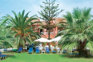 A hotel courtyard with palm trees, blue lounge chairs, and white umbrellas.