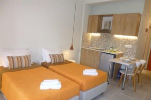 A hotel room with two beds, a small kitchenette, and a dining area.