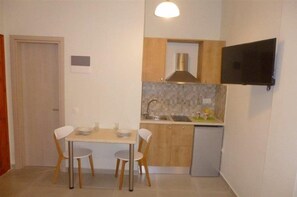 A compact kitchen with a dining table, two chairs, a sink, and a small refrigerator.