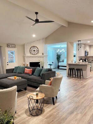A modern living room with a fireplace, a dining area with bar stools, and a kitchen with a bar. - Sparkling Springs - King Bed, Beauty, Charming, Family Fun (Houston)