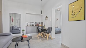 Ein modernes Wohnzimmer mit grauem Sofa, einem Esstisch mit vier Stühlen, einer Küchenzeile und einem großen, gelben Kunstwerk an der Wand.