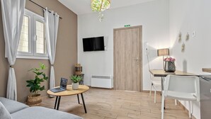 Ein modernes Wohnzimmer mit einer Couch, einem runden Holztisch, einem an der Wand befestigten Fernseher, einer Holztür und einer kleinen Pflanze.