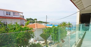 Zona residencial con vista a una piscina, una casa con techo de tejas rojas y un balcón con barandilla de vidrio.