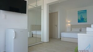 Una habitació d'hotel amb un llit, un televisor penjat a la paret, un refrigerador i un quadre d'un veler.