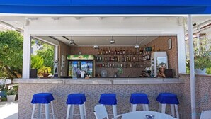 Zona de bar a l'aire lliure amb mur de maó, diverses ampolles i quatre tamborets blancs amb fons blaus.