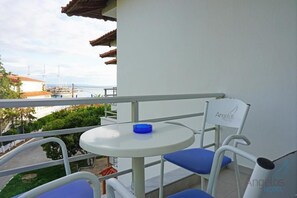 Un balcón con mesa y sillas, vista al mar, y un edificio con un cartel que dice "Angelos Hotel".