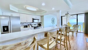 Une cuisine moderne avec des meubles blancs, des appareils en acier inoxydable et un comptoir-bar en bois, agrémenté de tabourets de bar.