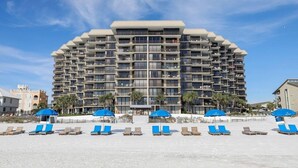 Un hôtel à plusieurs étages doté de balcons, situé en bord de mer et équipé de parasols.
