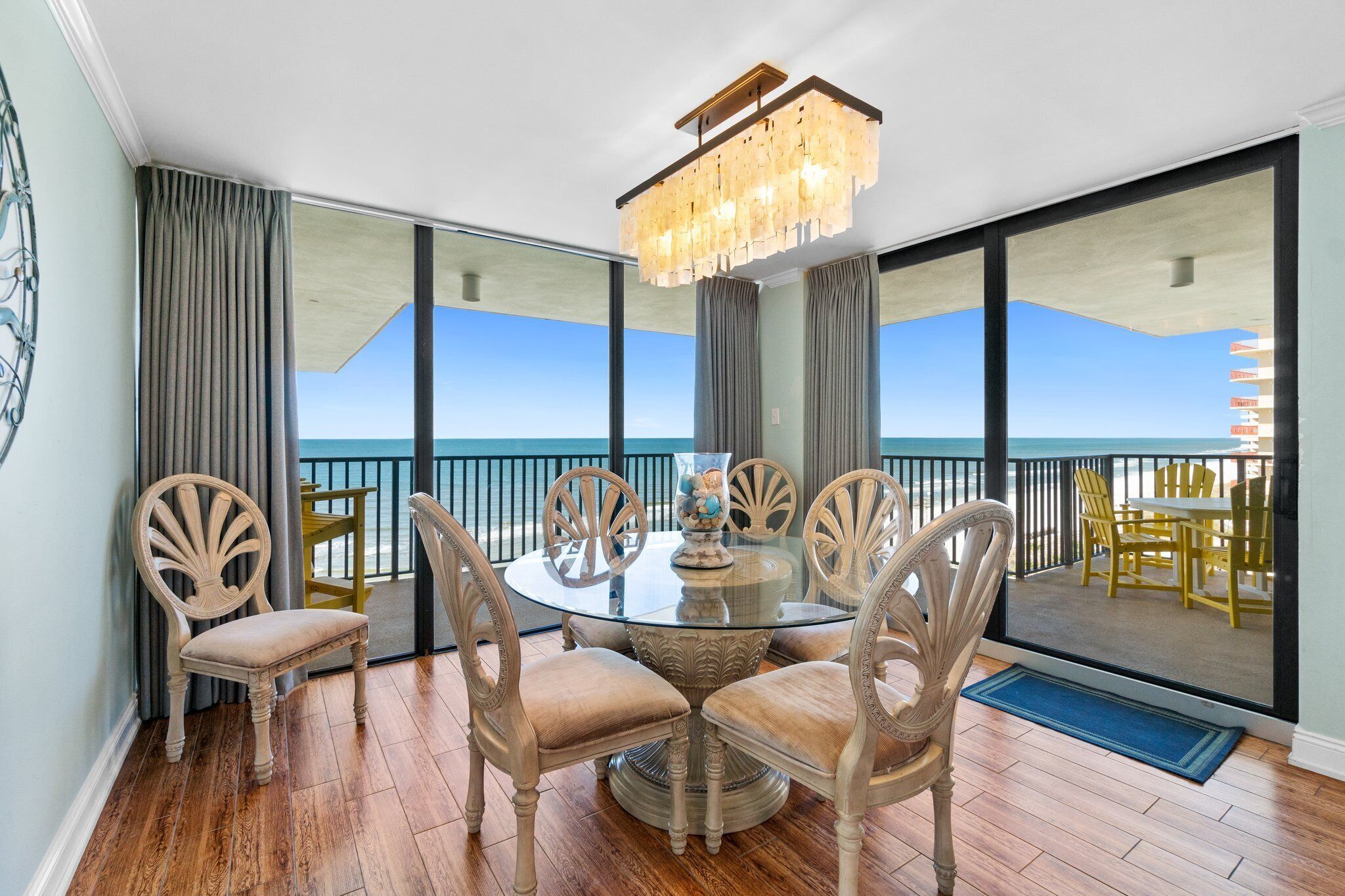 A dining area with a glass table and chairs, a chandelier, and a view of the ocean.