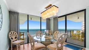 Un coin repas avec une table et des chaises en verre, un lustre et une vue sur l’océan.