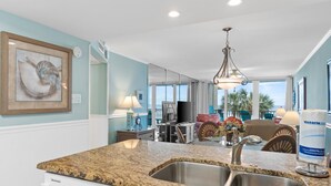 A kitchen with granite countertops, stainless steel sink, and a dining area with chairs and a table.