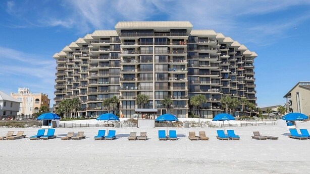 A multi-story hotel with balconies, a beachside location, and sun umbrellas.