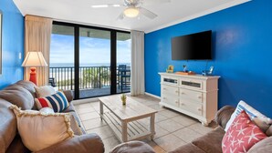 A living room with a sofa, a coffee table, a TV, and a balcony with a view.