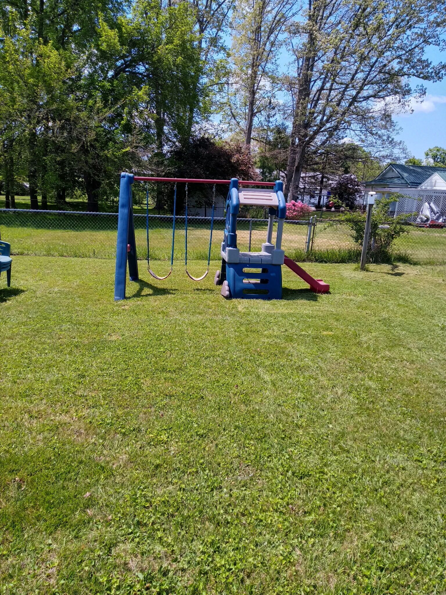 Une aire de jeux avec des balançoires et un toboggan, entourée d’herbe et d’arbres.