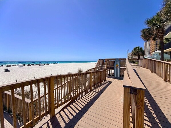 Ein Holzsteg führt zu einem Strand bei blauem Himmel.