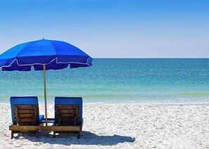 Une plage avec deux chaises longues en bois sous un parasol bleu.
