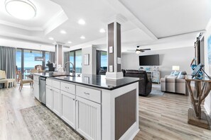 A modern living room with a large island, a flat-screen TV, and a view of the ocean. - Pelican Walk 308 Gulf Front Bliss! Free Chairs! (Panama City Beach)