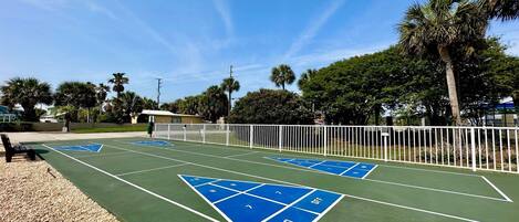 Ein Tennisplatz mit blauen Behindertenflächen, umgeben von einem weißen Zaun und Palmen.