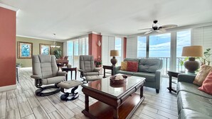 A spacious living room with a large window, a ceiling fan, and a dining area with a table and chairs.