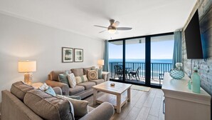 Una sala de estar con sofá, mesa de centro y ventilador de techo. Hay un balcón con vista al océano.