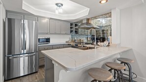 Una cocina moderna con un refrigerador de acero inoxidable, una isla de mármol y taburetes de bar.
