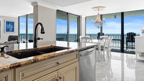 Una cocina moderna con una isla grande, lavavajillas y vistas al océano a través de amplios ventanales.