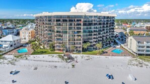 A multi-story hotel with a central courtyard, surrounded by a sandy beach and clear blue sky.