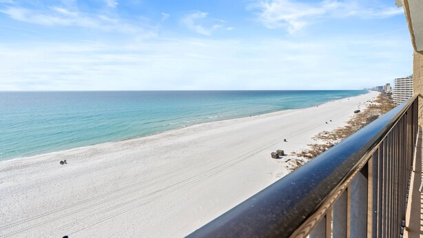 Vista de la playa desde un balcón con barandilla, una playa arenosa y un cielo azul despejado.