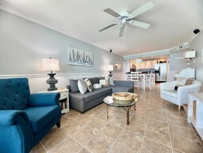 A living room with a blue sofa, a grey sofa, a white armchair, a coffee table, and a ceiling fan.
