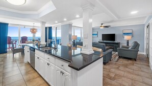 A spacious living area with a kitchen island, a dining area with a view, and a seating area with a TV and lamp.