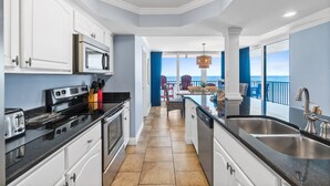 A modern kitchen with white cabinets, a stainless steel sink, and a view of the ocean through large windows.