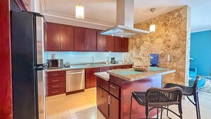 A modern kitchen with dark wooden cabinets, stainless steel appliances, and a central island with bar stools. - Incredible 3 BR Penthouse w BBQ & Jacuzzi (Punta Cana)