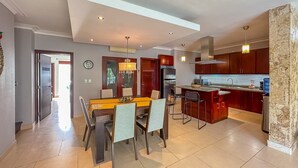 A modern kitchen with dark wooden cabinets, a central island, and a dining area with a table and chairs. - Incredible 3 BR Penthouse w BBQ & Jacuzzi (Punta Cana)