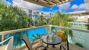 A rooftop pool area with a glass table and chairs, surrounded by lush greenery and modern buildings in the background. - Incredible 3 BR Penthouse w BBQ & Jacuzzi (Punta Cana)