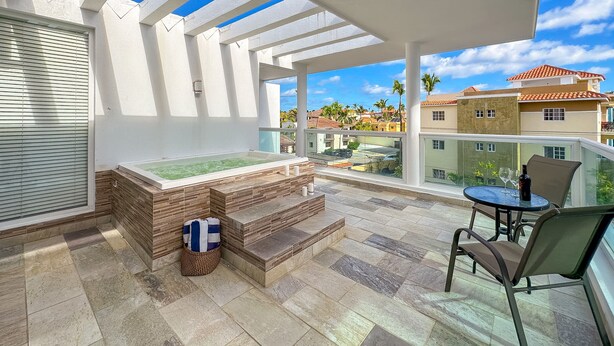 A balcony with a hot tub, a table with chairs, and a view of neighboring buildings. - Incredible 3 BR Penthouse w BBQ & Jacuzzi (Punta Cana)